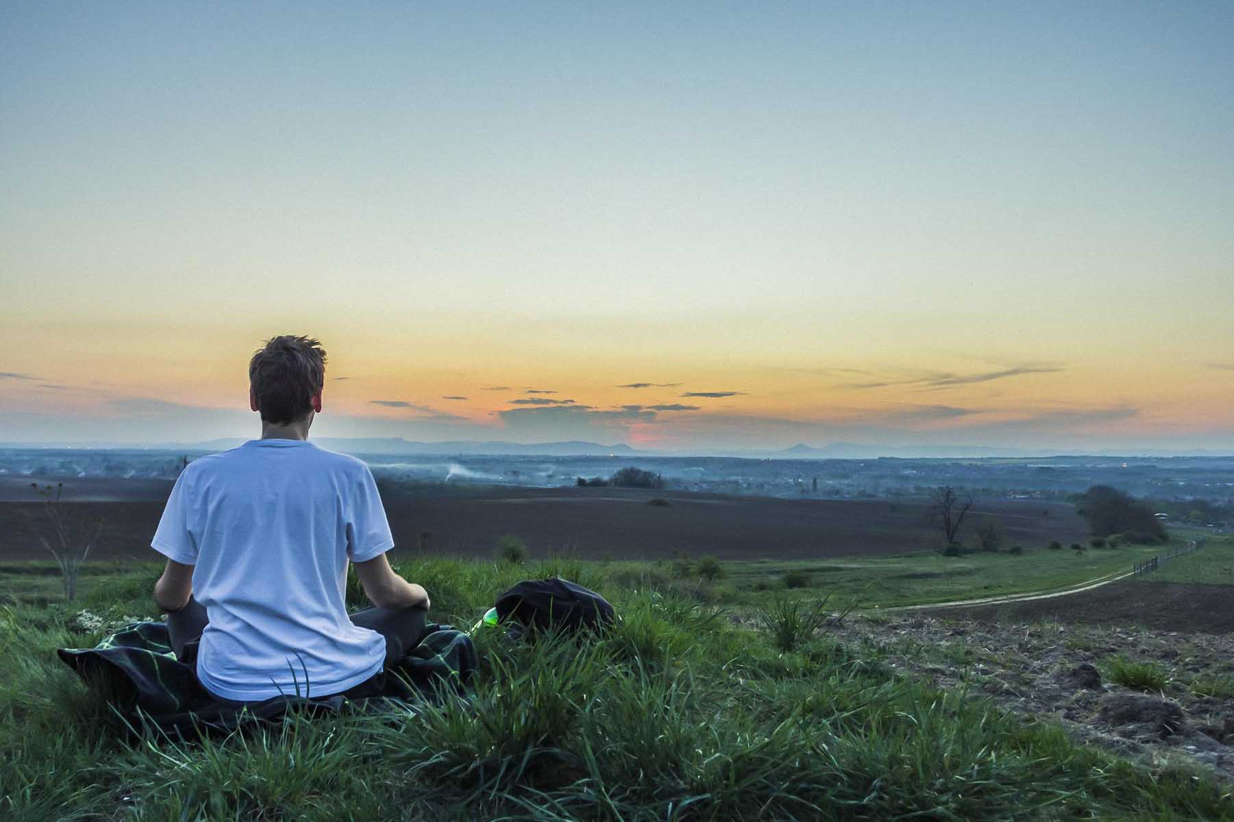 Man sitting on hill meditating at sunset
